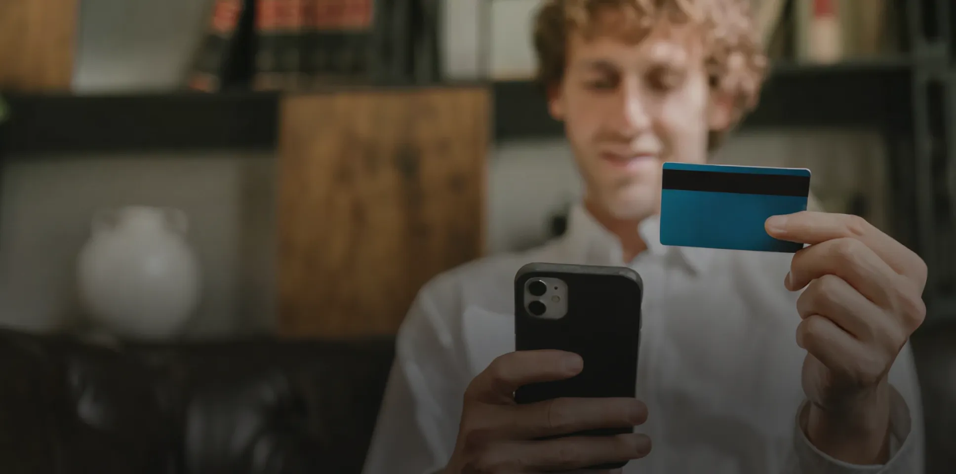 Hombre sosteniendo una tarjeta azul y usando un teléfono inteligente, posiblemente para una compra en línea.