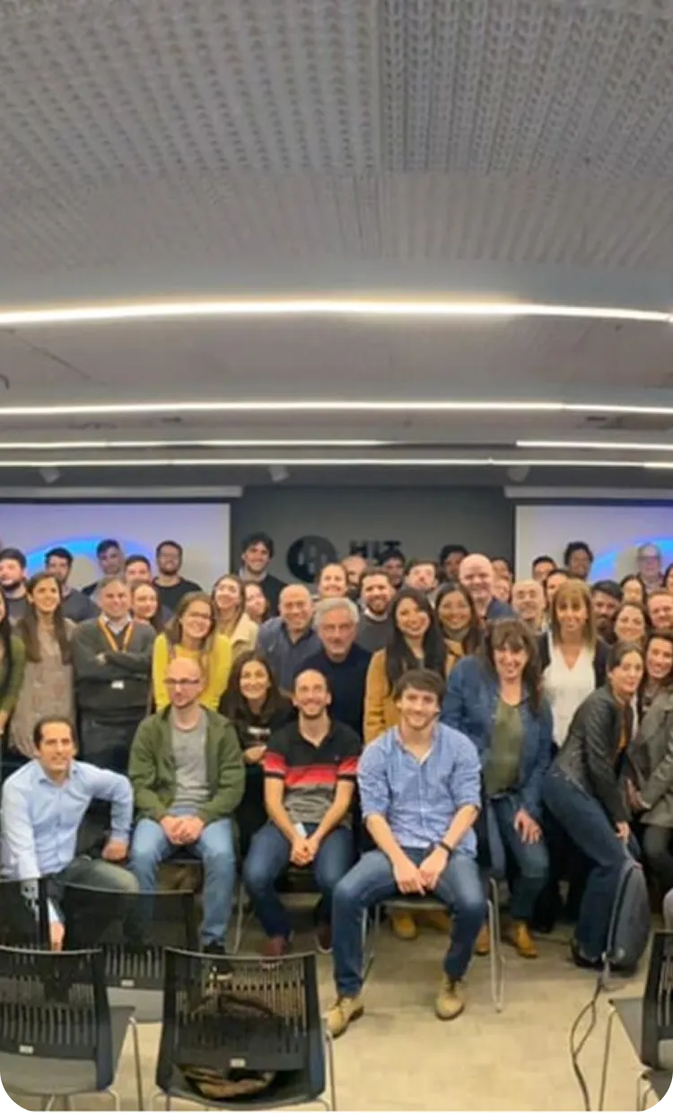 Gran grupo de personas en una sala de reuniones moderna con luces curvas en el techo y varias sillas vacías al frente.