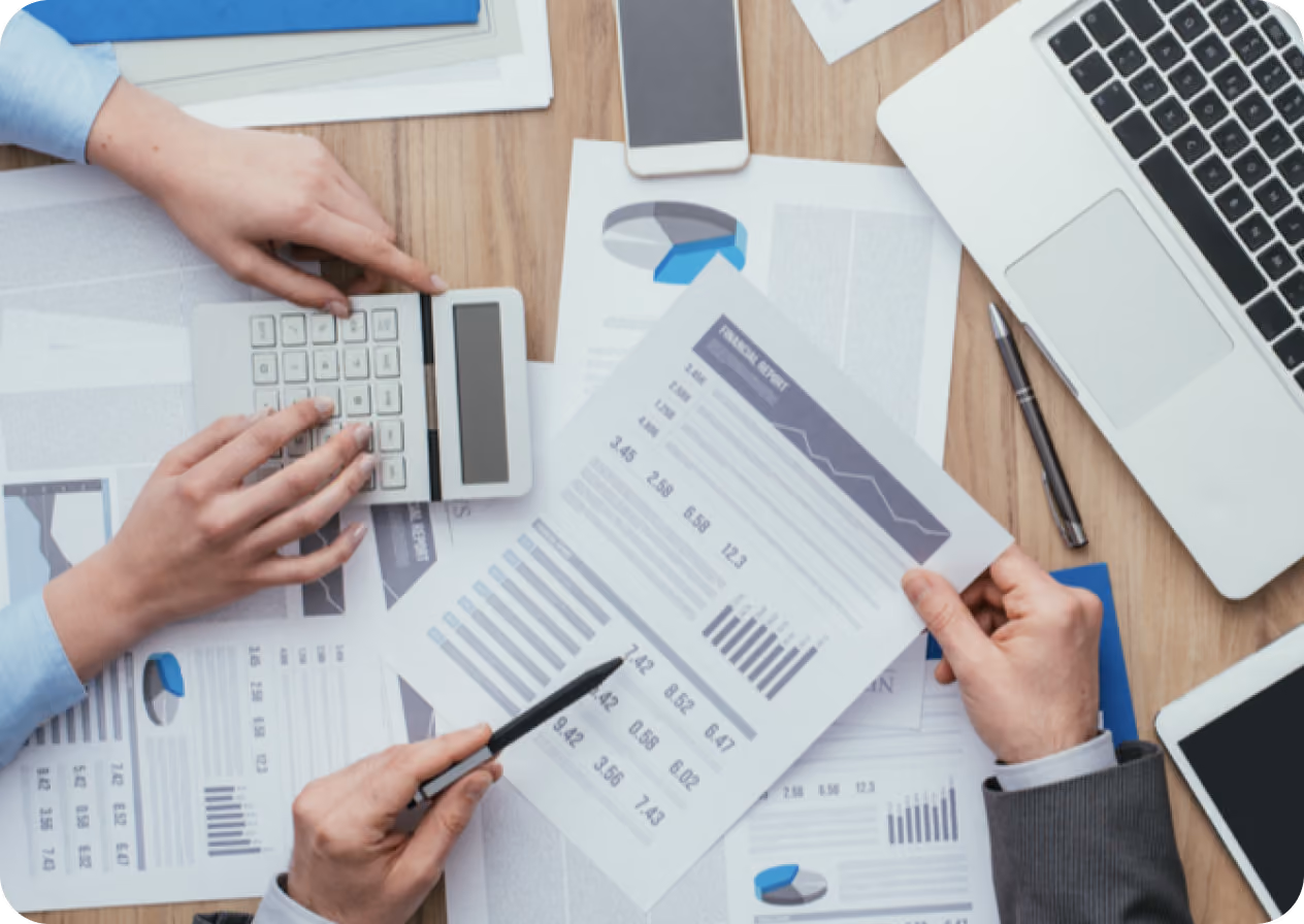 Personas analizando gráficos y datos financieros sobre una mesa con calculadora y laptop.