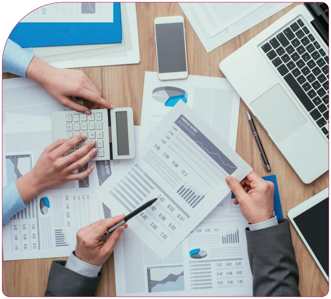Personas analizando gráficos y datos financieros sobre una mesa con calculadora y laptop.