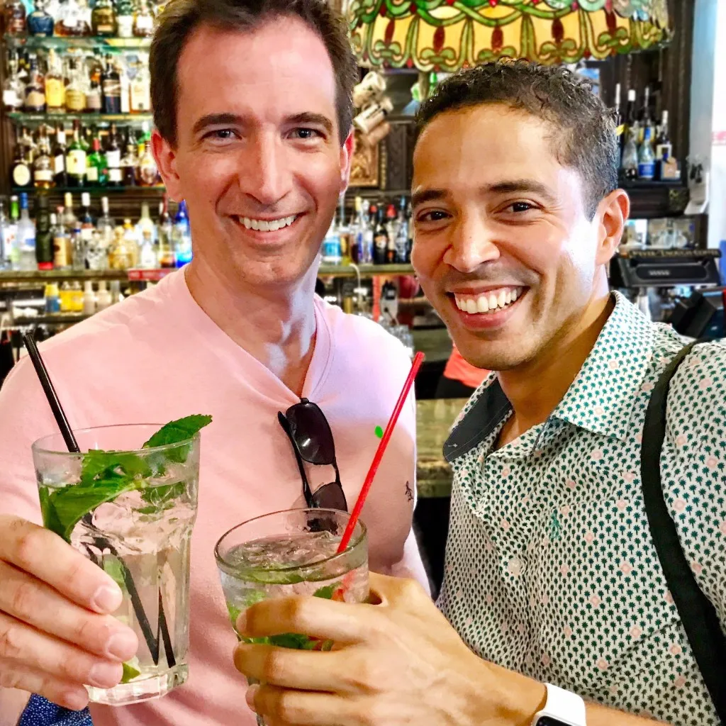 Two smiling men holding glasses with mojito cocktails in a bar setting.
