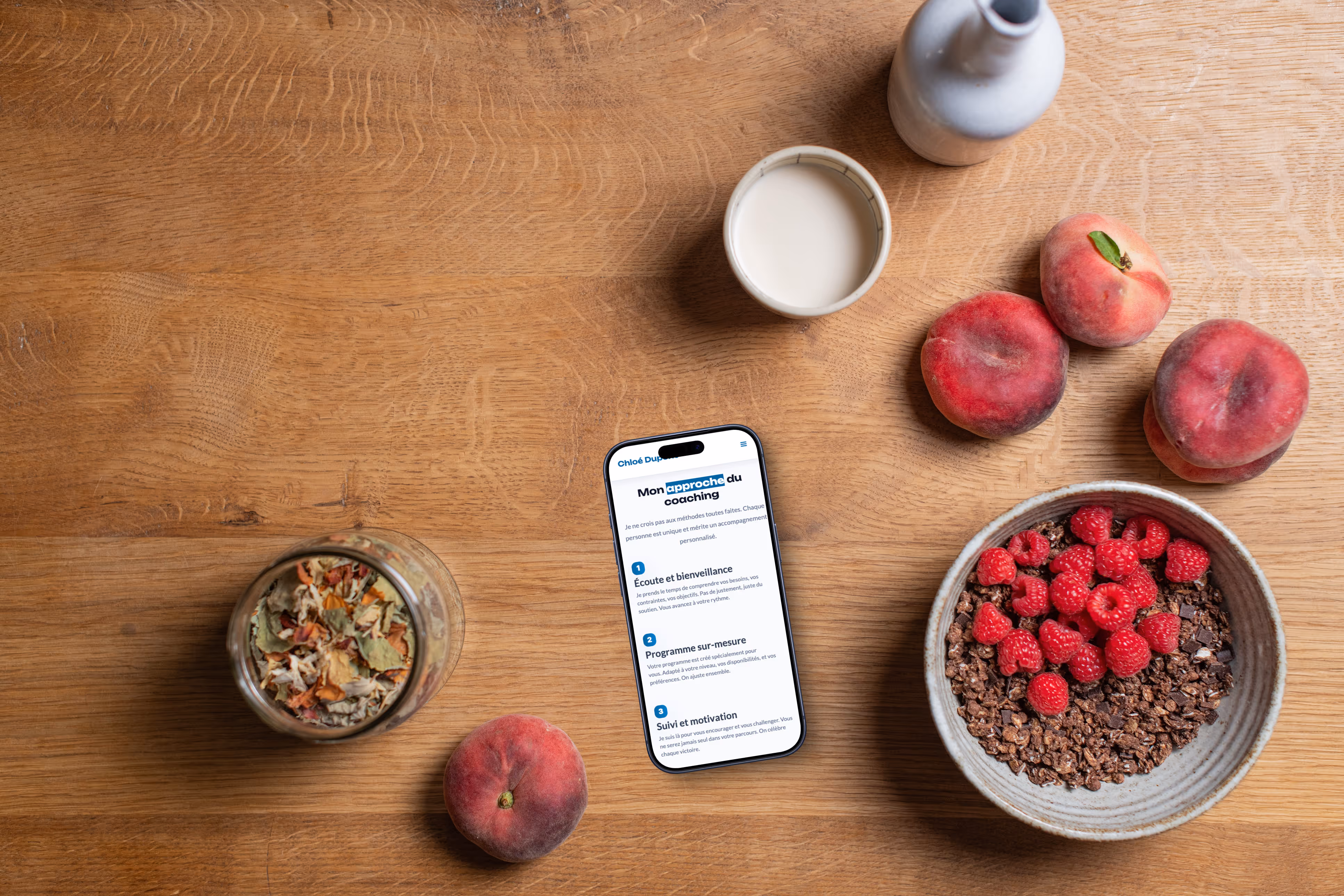 Mise en scène d'un mobile posé une table entouré de fruits affichant la page "mon approche du coaching" du site coach