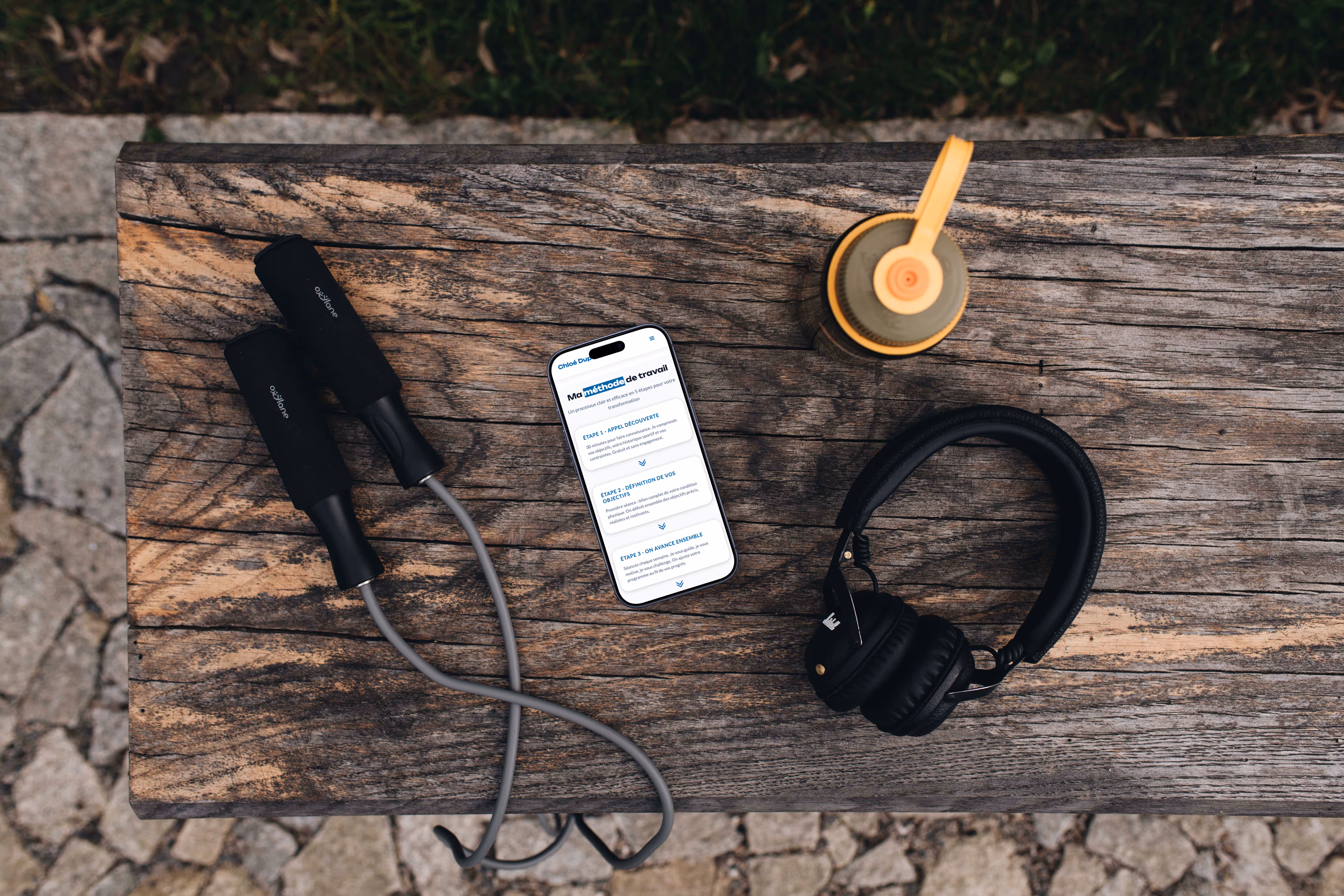 Mise en scène d'un mobile posé sur un banc entouré d'accessoires de sport affichant la page "ma méthode de travail" du site coach