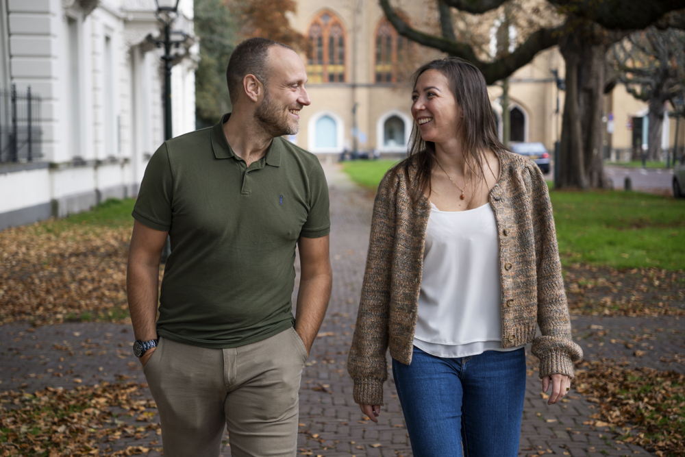 Man en vrouw wandelen buiten op een herfstpad en lachen naar elkaar.