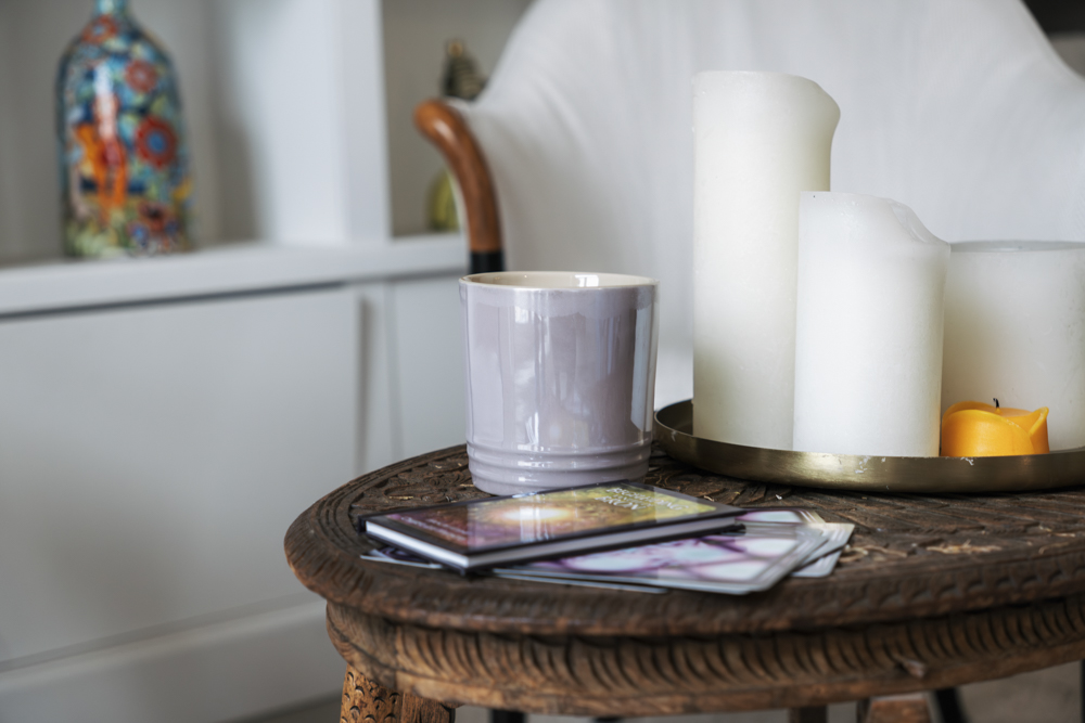 Houten tafel met een grijze mok, een stapel tarotkaarten en een houten dienblad met grote witte kaarsen en een kleine gele kaars.
