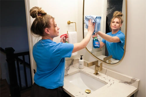 cleaner wiping a bathroom mirror