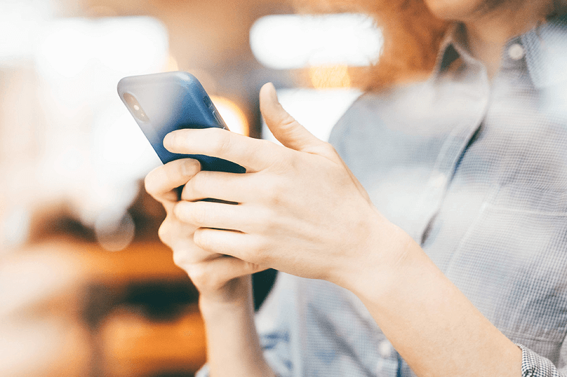 Primer plano de una mujer utilizando un smartphone con ambas manos en un ambiente con iluminación cálida.