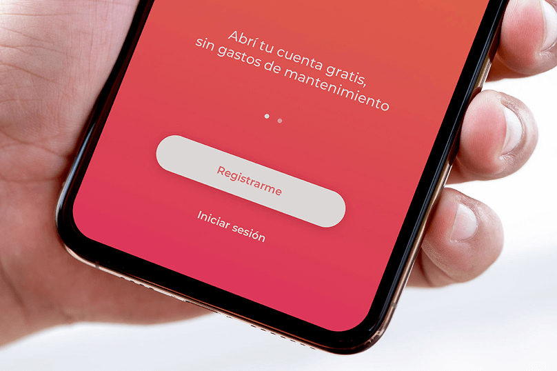 Primer plano de una mano sosteniendo un celular con la pantalla de inicio de la aplicación de Banco del Sol, destacando el botón "Registrarme" sobre un fondo rojo degradado.