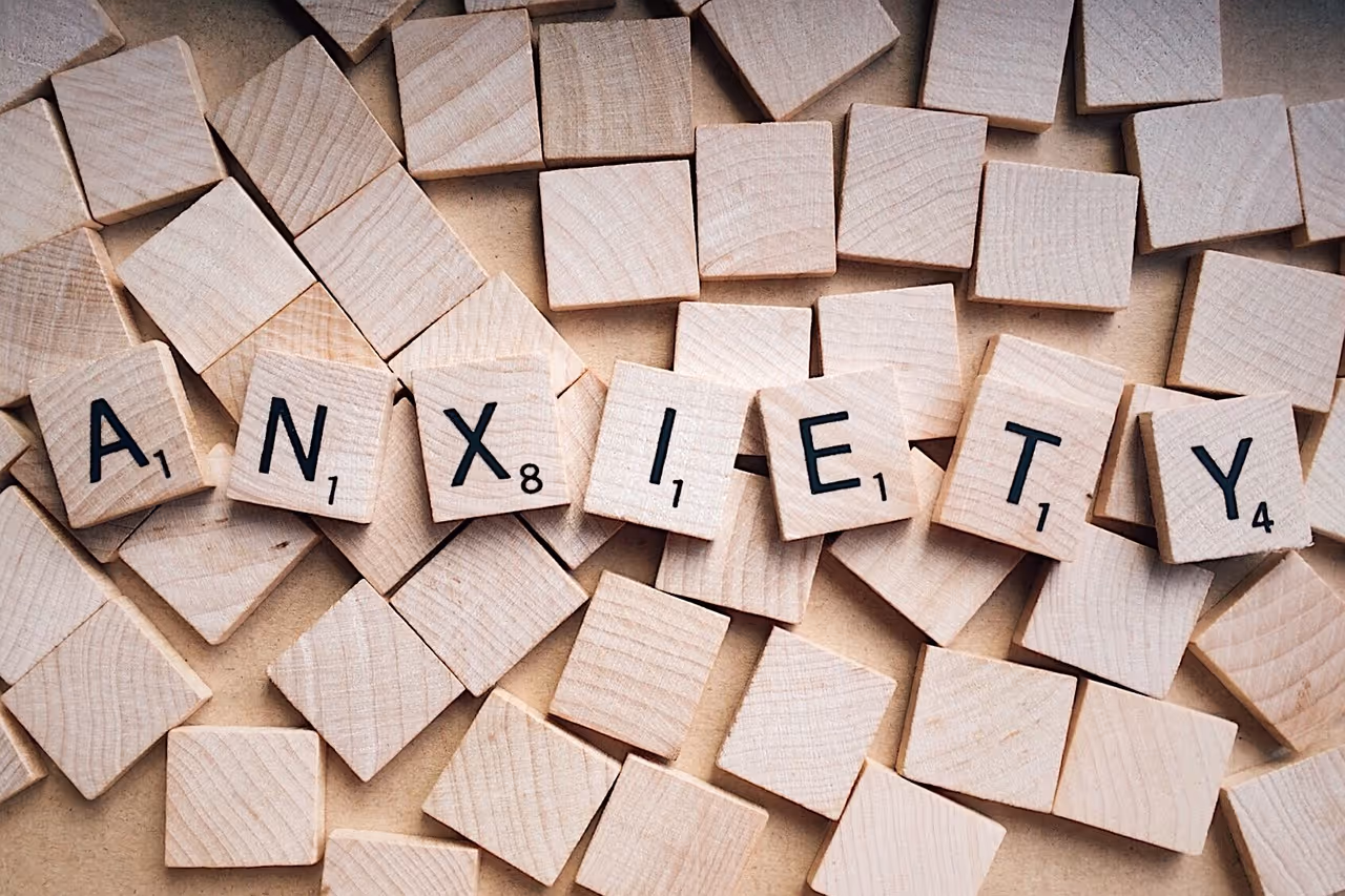 Wooden Scrabble tiles spelling the word 'ANXIETY' on scattered blank tiles.
