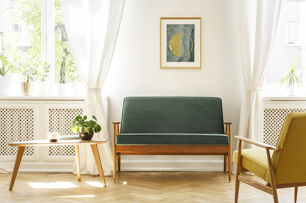 Bright living room with a green velvet loveseat, yellow armchair, wooden coffee table, plants, and framed wall art.