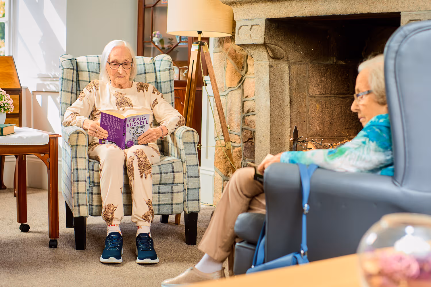 Two elderly women sitting in armchairs in a cozy living room.