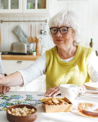 An elderly woman and her carer sit at a table and work on a puzzle