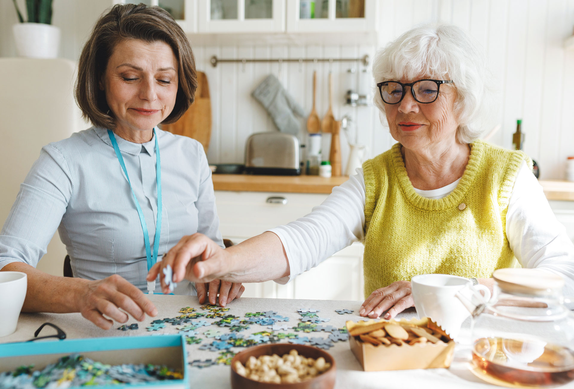 An elderly woman and her carer sit at a table and work on a puzzle