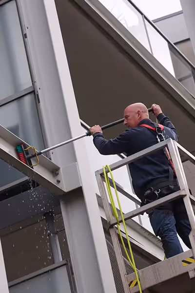 Asito-medewerker voert constructiereiniging uit op hoogte met hogedrukunit en veiligheidslijn.