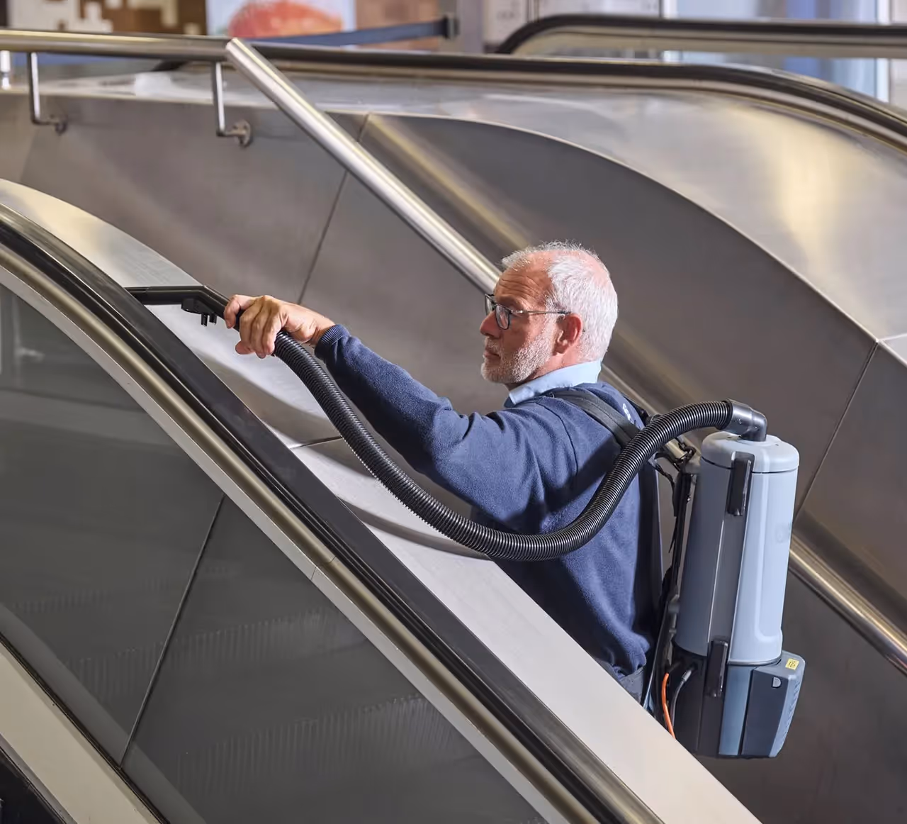 Asito-medewerker reinigt de leuning van een roltrap met een speciale stofzuiger voor een veilige en hygiënische uitstraling