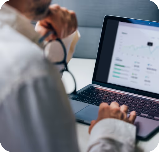 Person reviewing health data charts on a laptop screen, seated at a desk in a clinical setting.