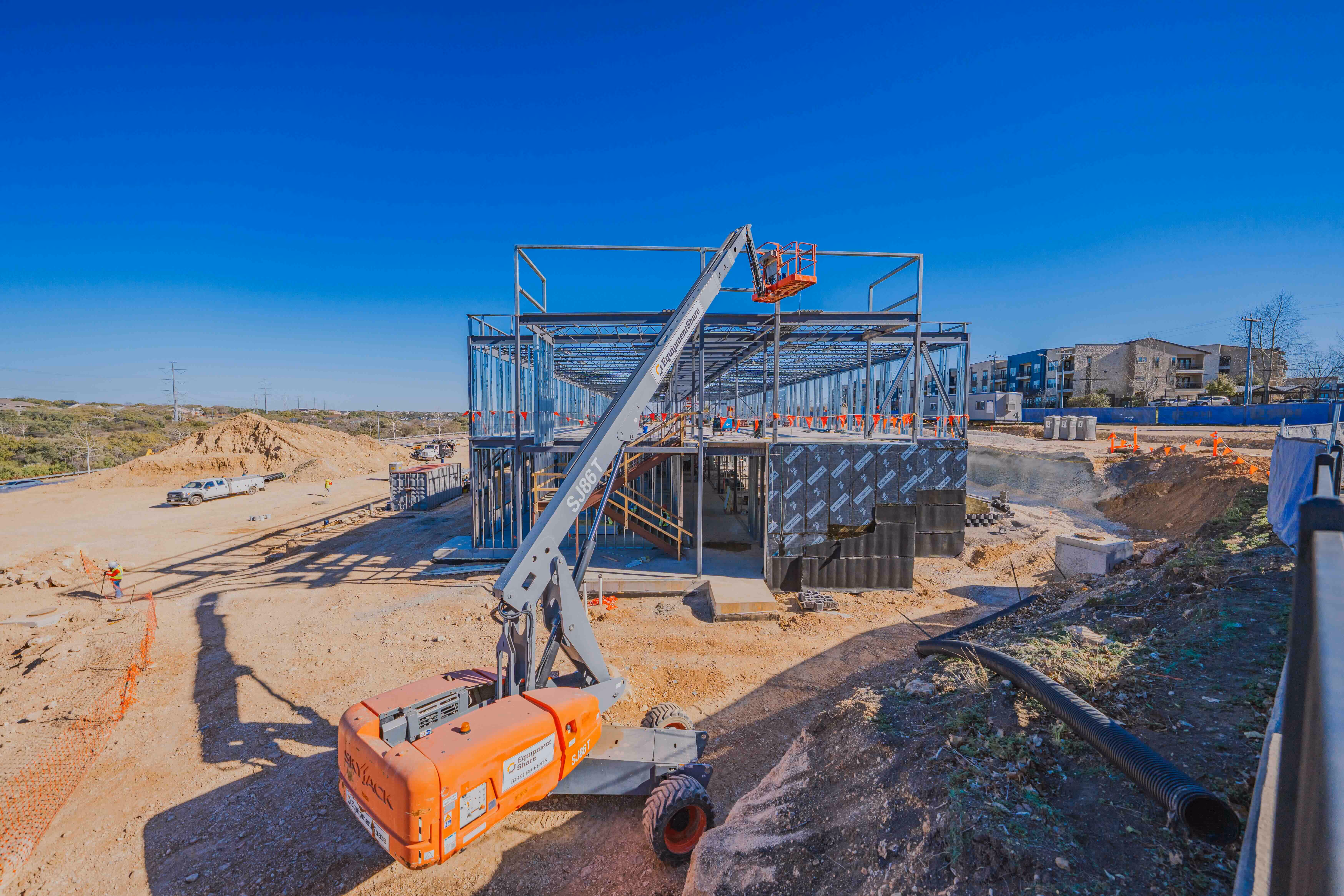 Construction site with a steel frame building under construction and an orange lift machine in front.