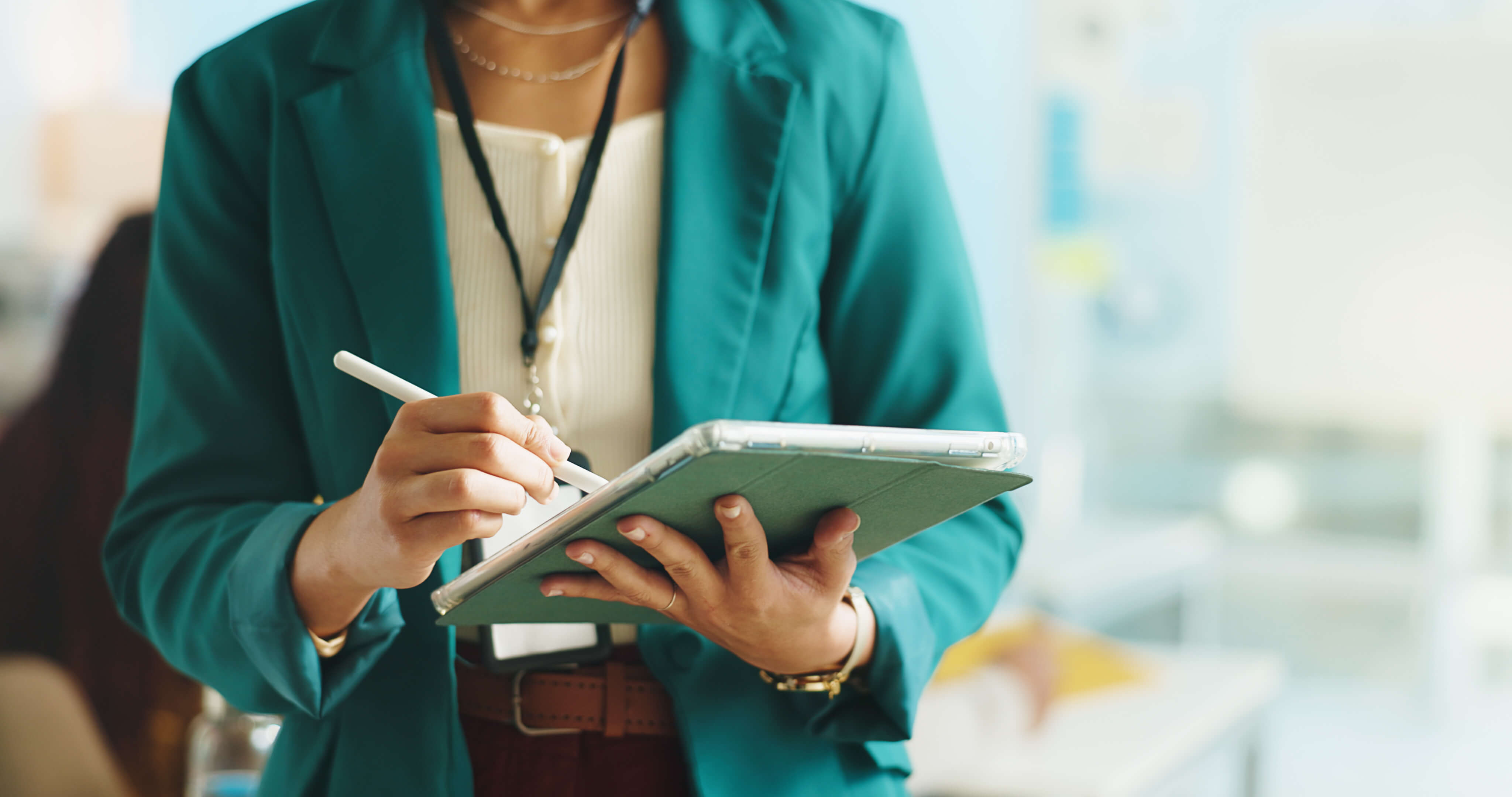 Person in teal blazer holding a tablet and using a stylus pen.