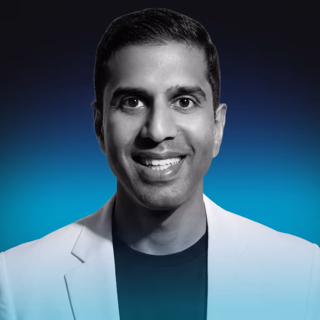 Smiling man with short dark hair wearing a light-colored blazer over a dark shirt against a blue gradient background.