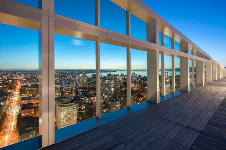 Rooftop patio with wood flooring and glass panels offering a city skyline view at dusk.