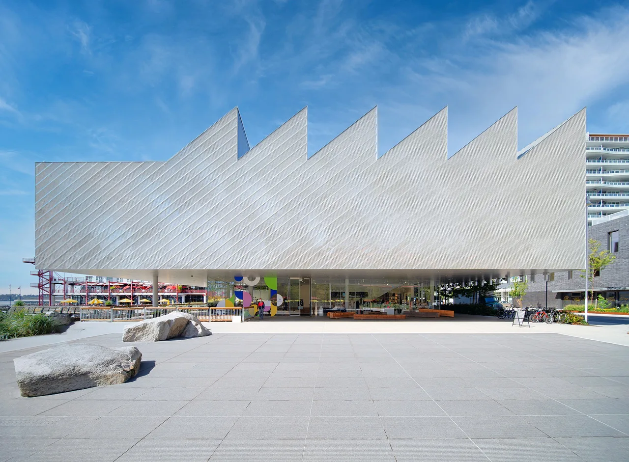 Modern building with a sawtooth roof design and large glass windows, set against a blue sky.