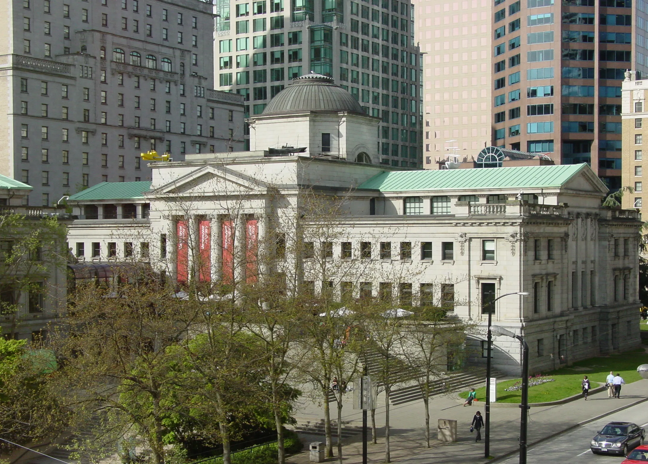 Vancouver Art Gallery building with classical architecture and green roofs, surrounded by trees and urban skyscrapers.