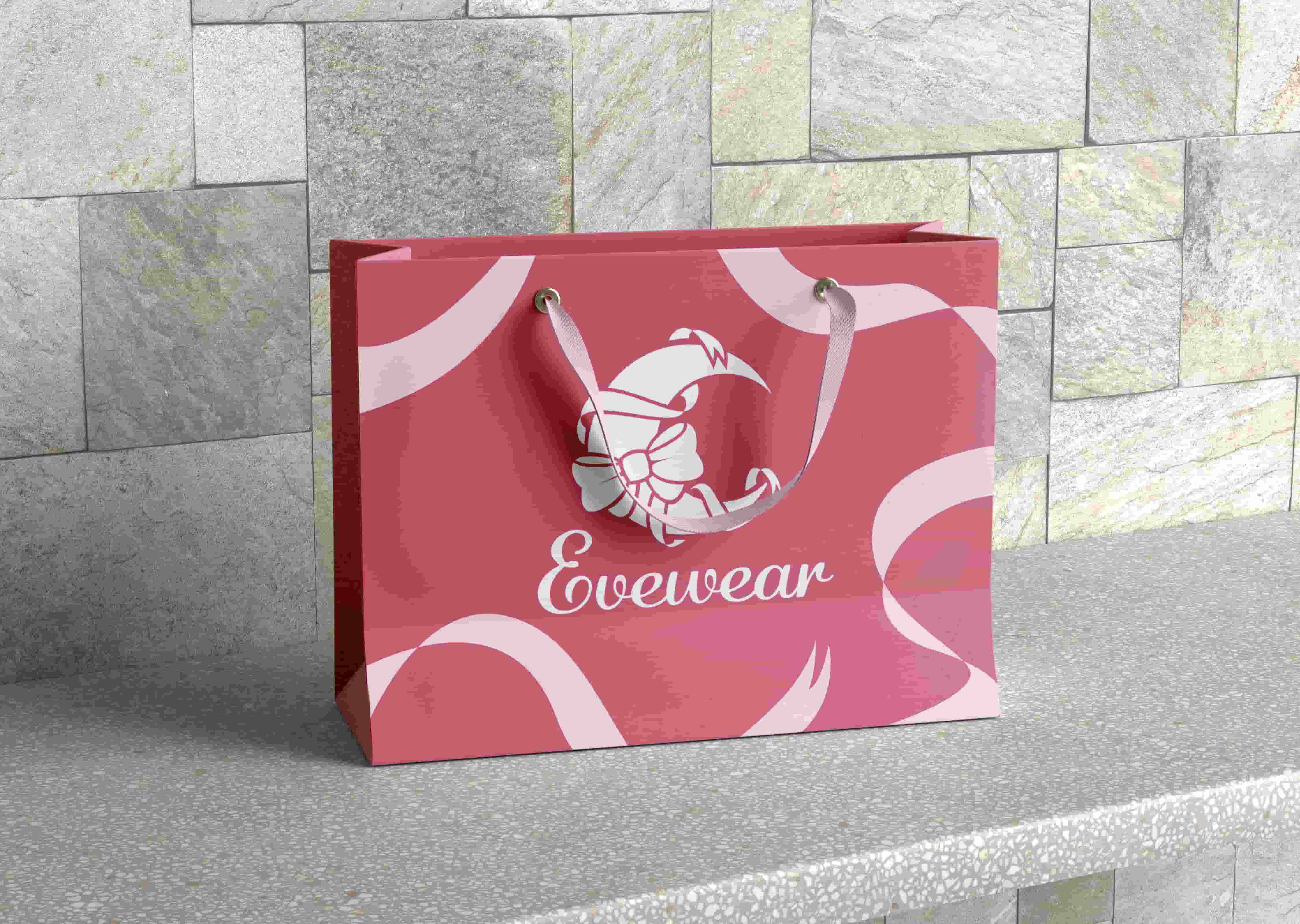 Red and pink shopping bag with the brand name 'Evewear' and a stylized flower logo, placed on a textured stone surface with a stone tile background.