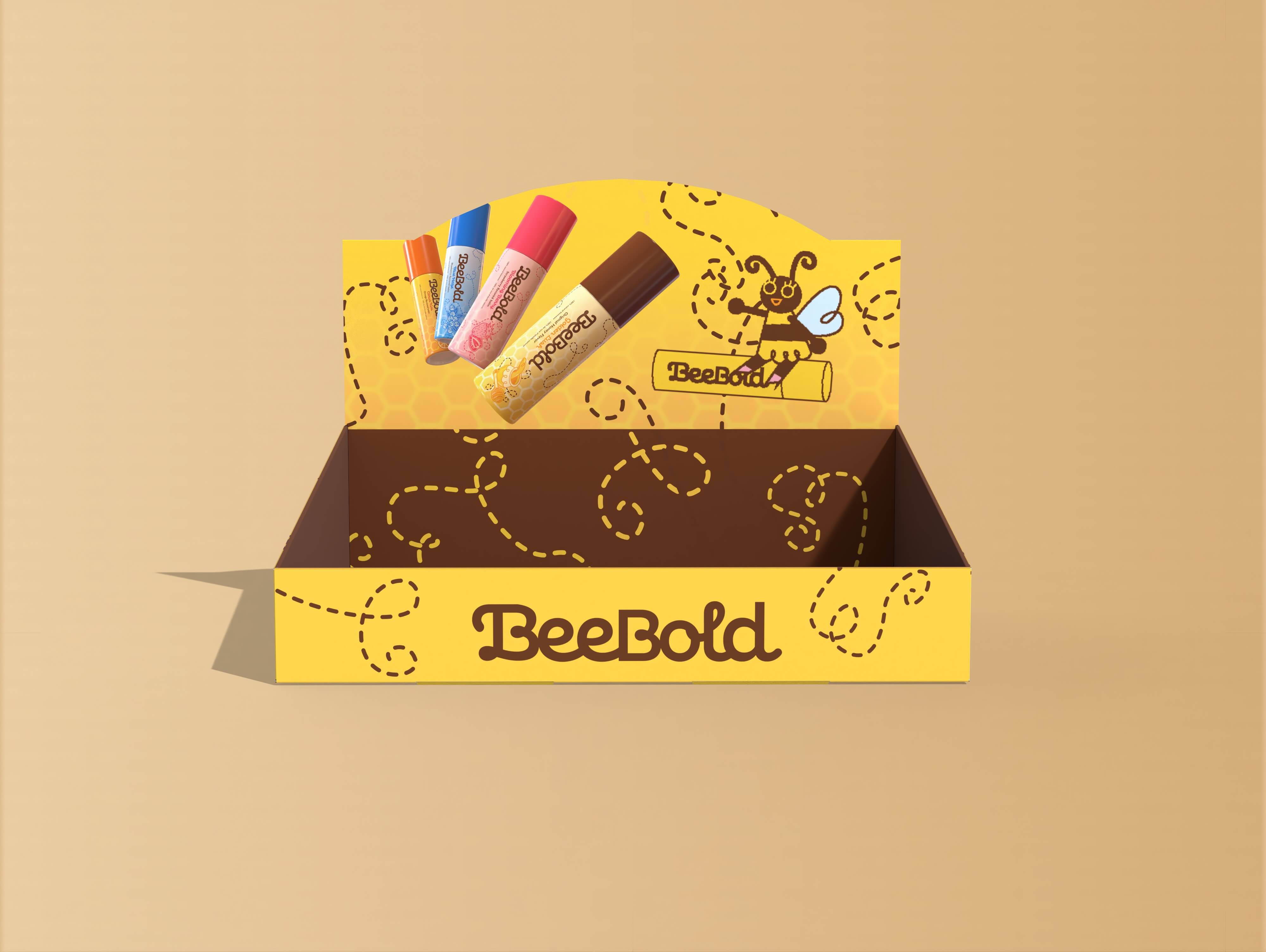 Yellow and brown BeeBold branded display box with decorative bee and four colorful BeeBold lip balm tubes floating above.
