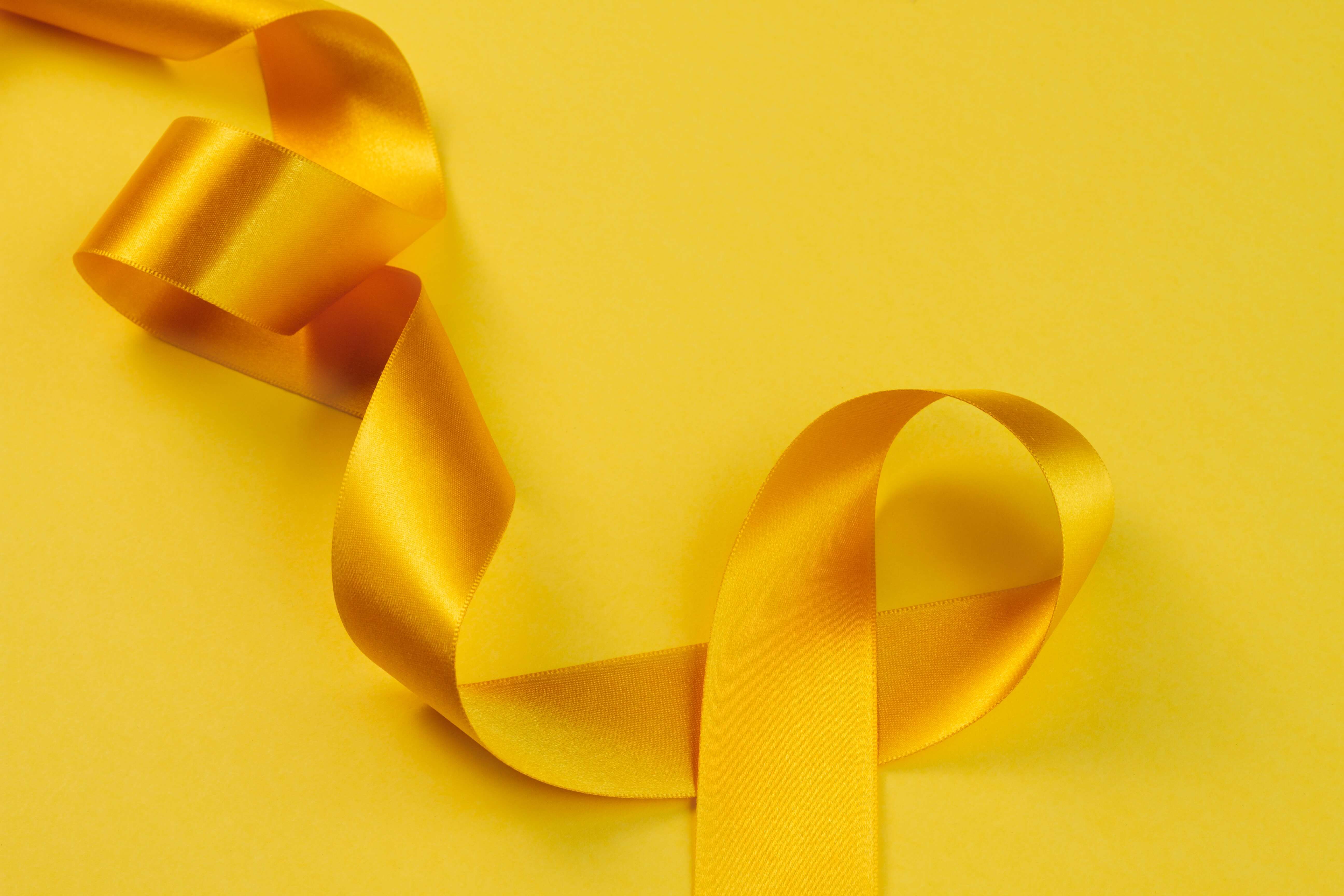 Shiny yellow satin ribbon twisted on a yellow background.