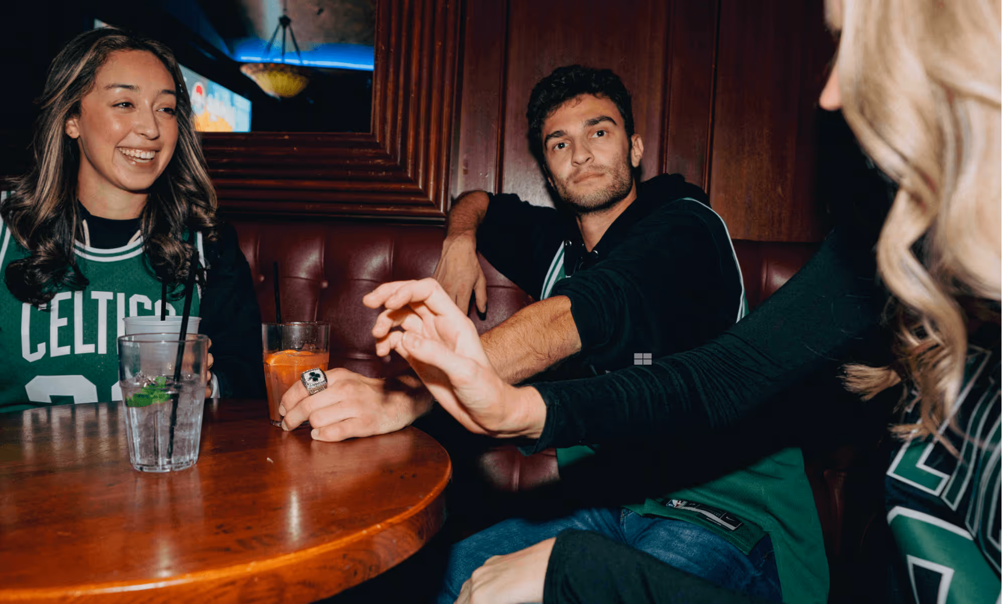 Friend group in Boston Celtics basketball jerseys sitting together in a dimly lit bar