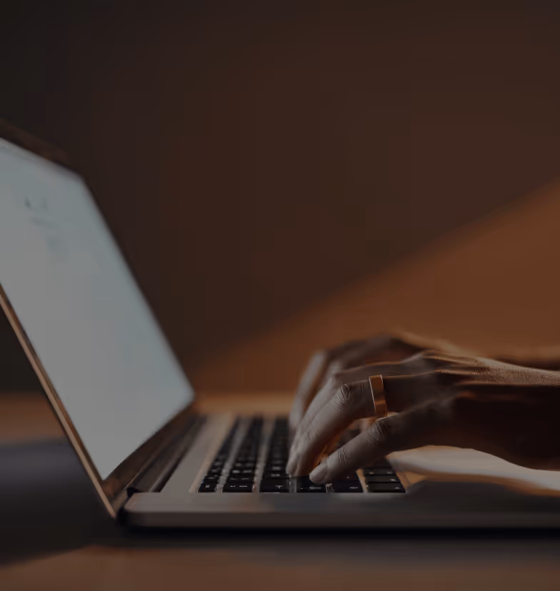 Close-up of hands typing on a laptop keyboard in low warm lighting.