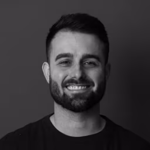 Smiling man with short dark hair and beard against a dark background.