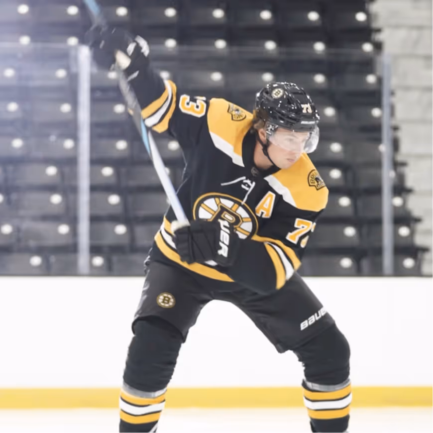 Hockey player in black and yellow Boston Bruins uniform preparing to shoot the puck on the ice rink.