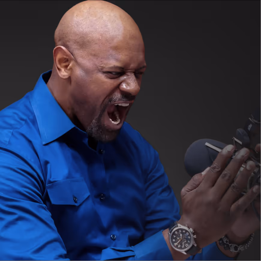 Man in blue shirt angrily shouting into a microphone with hands raised.