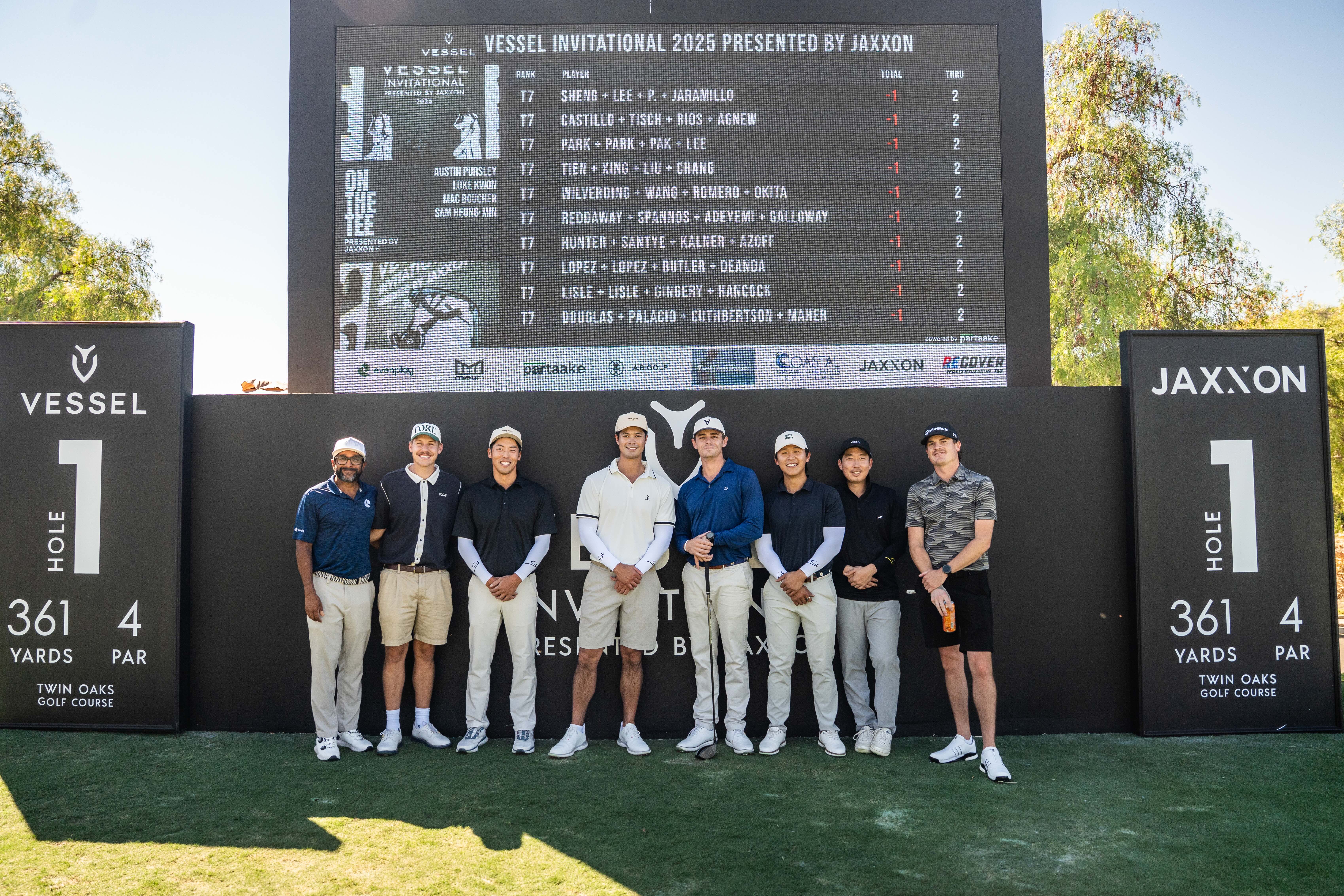 Eight male golfers standing on grass in front of a leaderboard and signage for Vessel Invitational 2025 at Twin Oaks Golf Course, Hole 1.