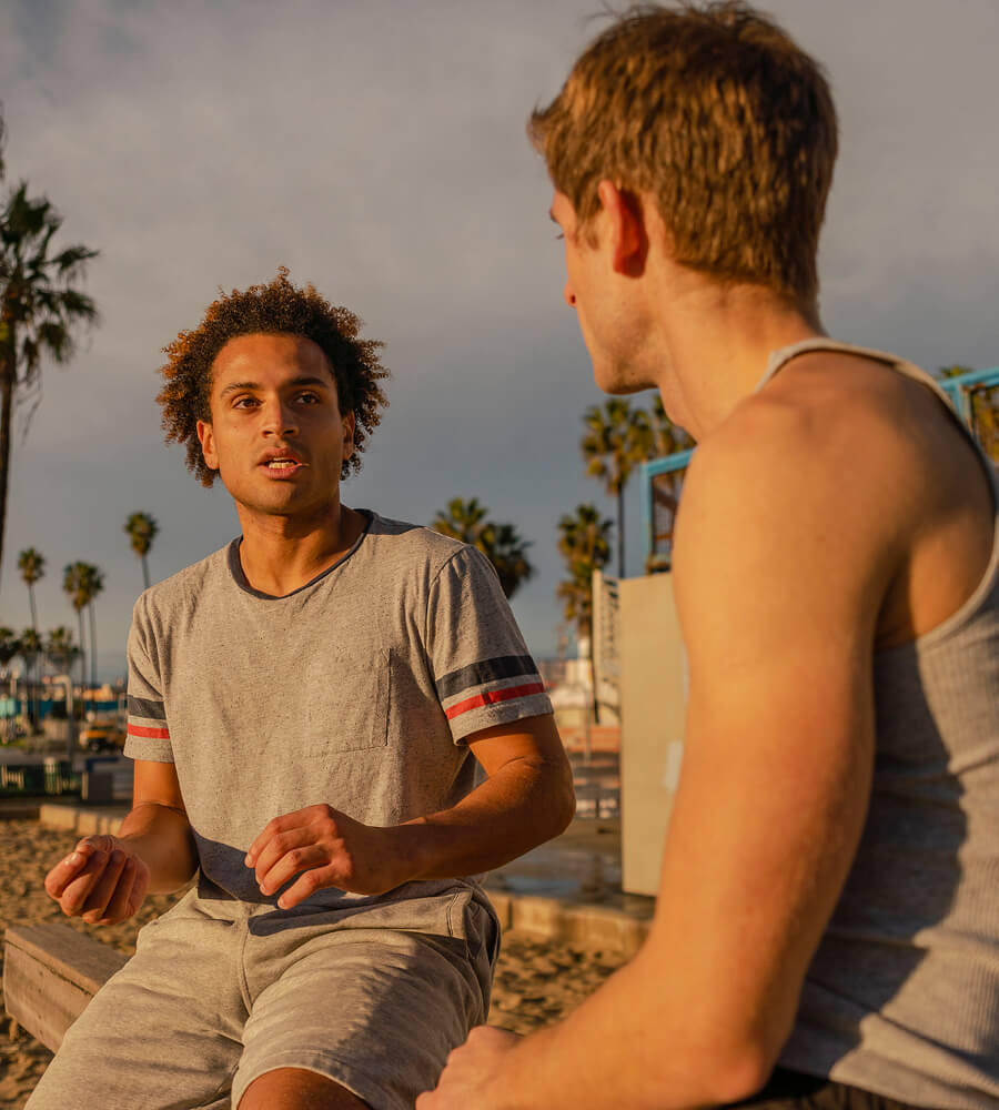 Two young men talking to each other, sitting outside