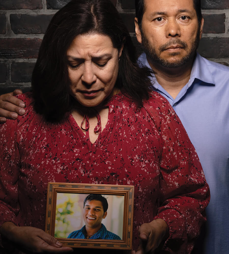 A mother and a father holding a photograph of their son, looking sad