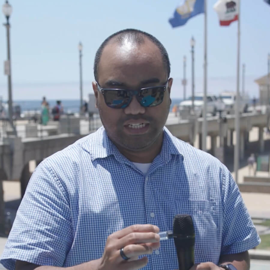 Man holding vial in front of the beach talking to person with microphone