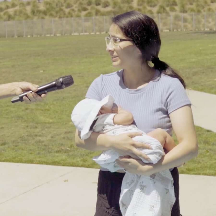 Mother holding baby outside while talking to person with microphone