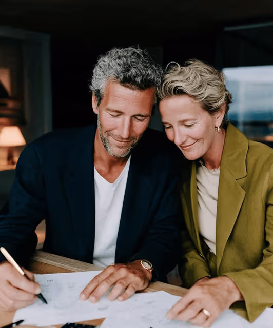 Un couple souriant signe des documents ensemble à une table dans une ambiance chaleureuse.