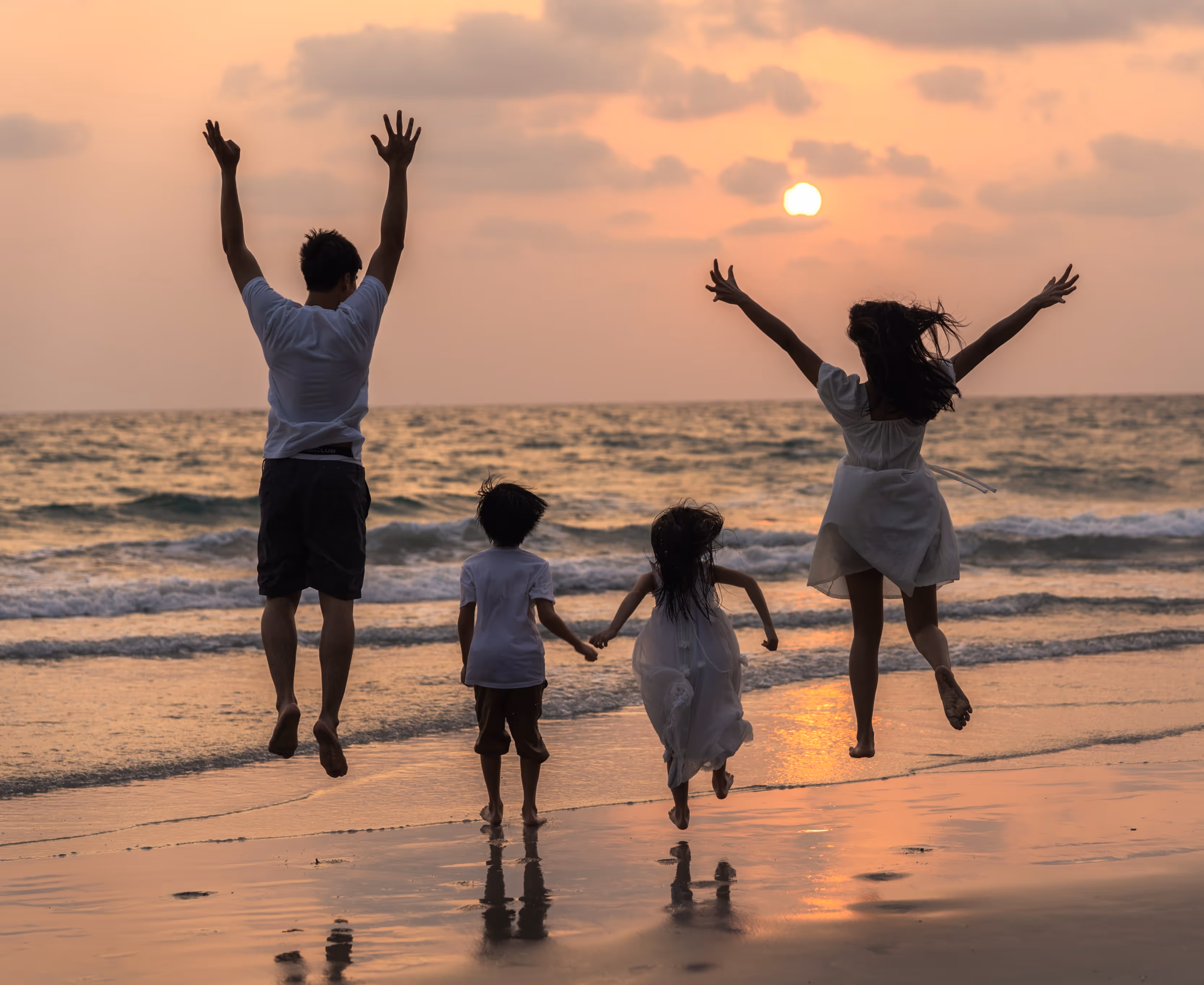 Famille heureuse sautant pieds nus sur une plage au coucher du soleil avec l'océan en arrière-plan.