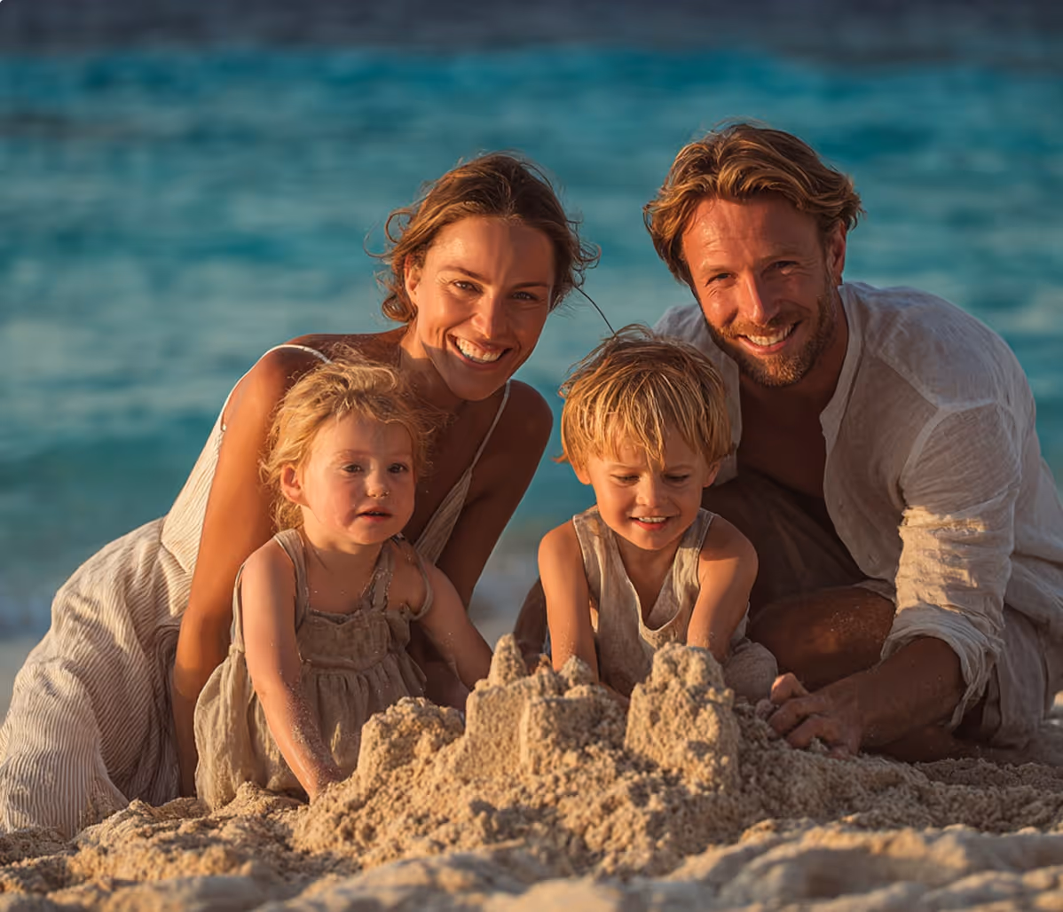 Famille souriante de deux adultes et deux enfants jouant à construire un château de sable sur la plage au bord de la mer.