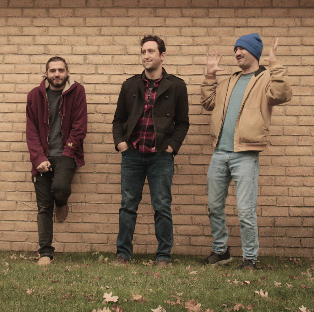 Band members of Space Turtles, standing in front of a tan brick wall.