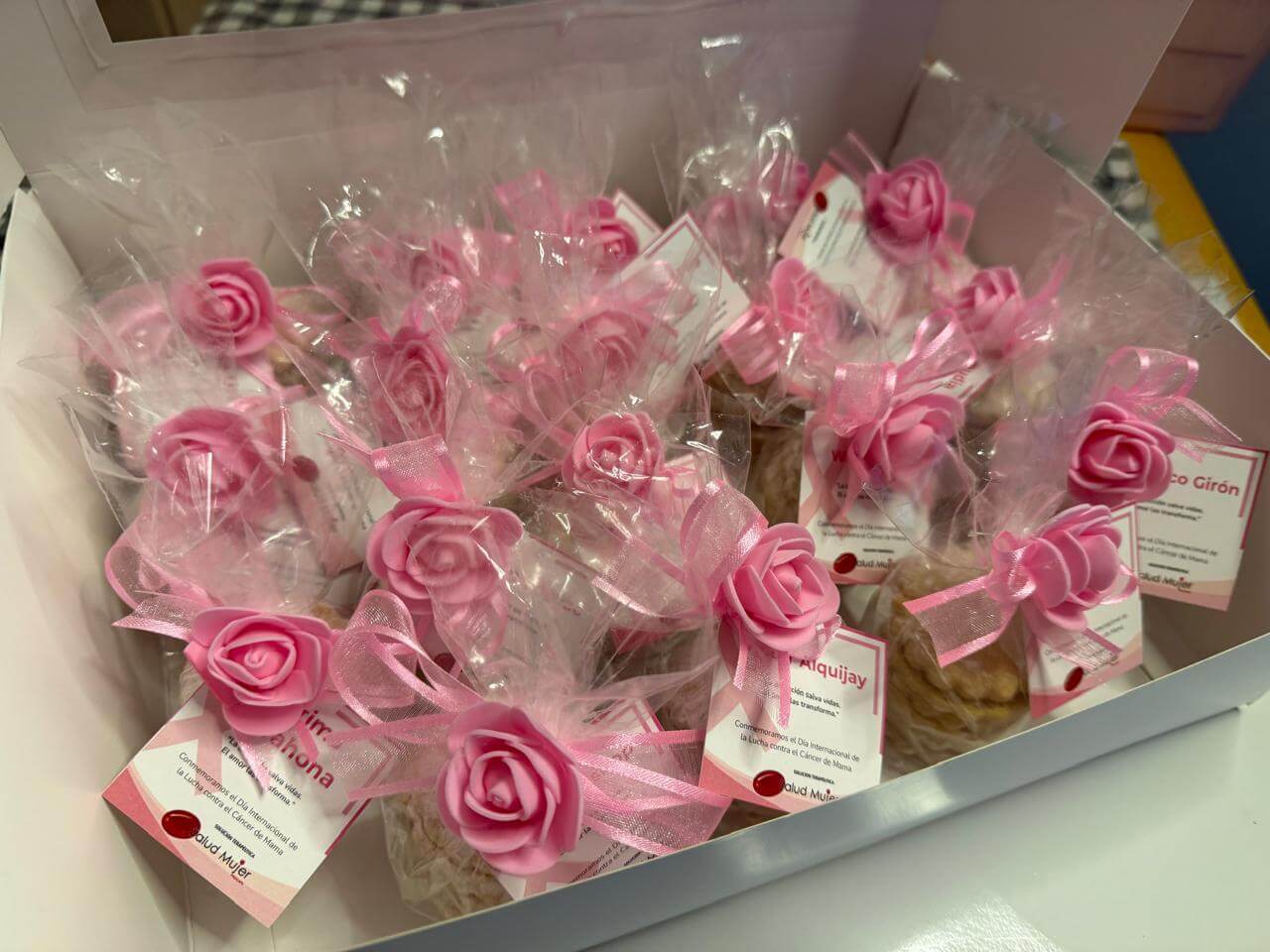 Box containing individually wrapped treats decorated with pink rose ribbons and tags commemorating International Breast Cancer Awareness Day.