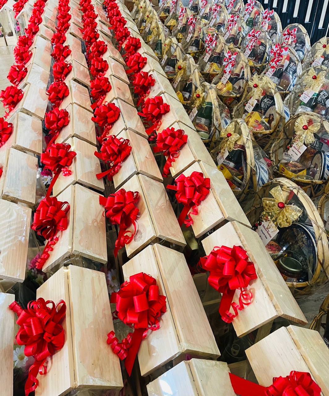 Rows of wooden gift boxes with red bows alongside wrapped gift baskets decorated with gold bows.