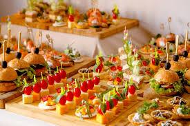 Variety of appetizers and mini sandwiches on wooden serving trays for a buffet event.