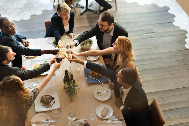 Six diverse adults sitting around a dining table clinking wine glasses in a cheerful toast.
