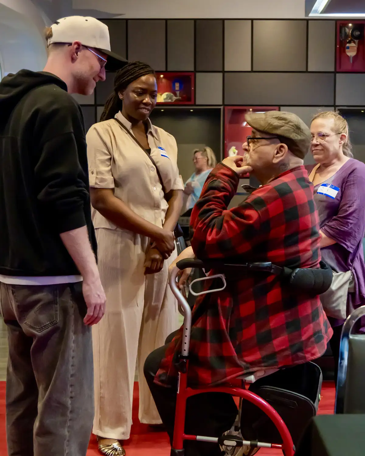 Four diverse adults engaging in conversation in a modern indoor setting with red flooring and black panel walls.