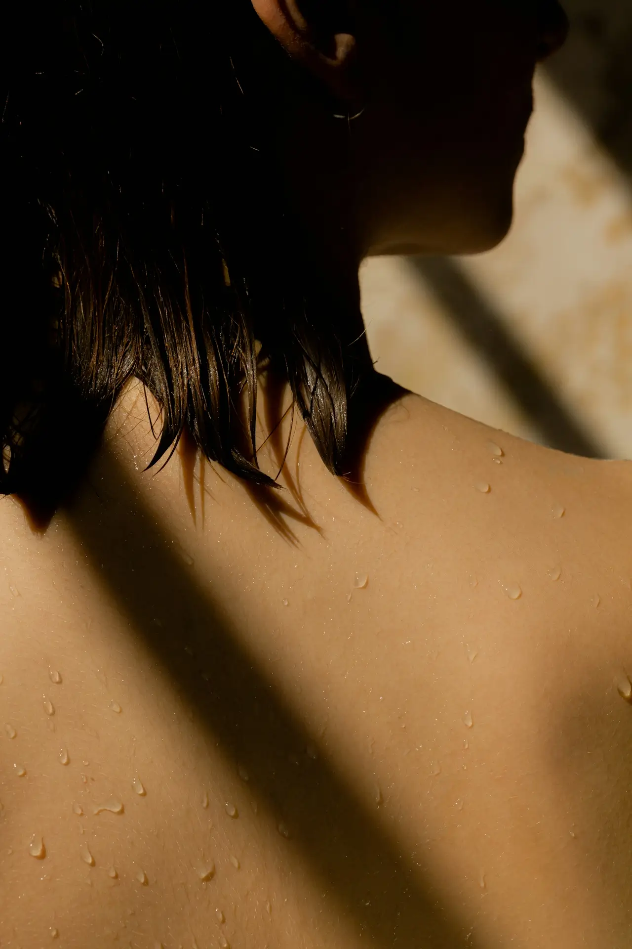 Close-up of a wet person's shoulder and neck with water droplets and wet hair, partially in shadow.