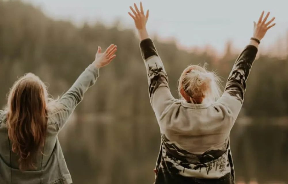 Two women in sweaters raising hands